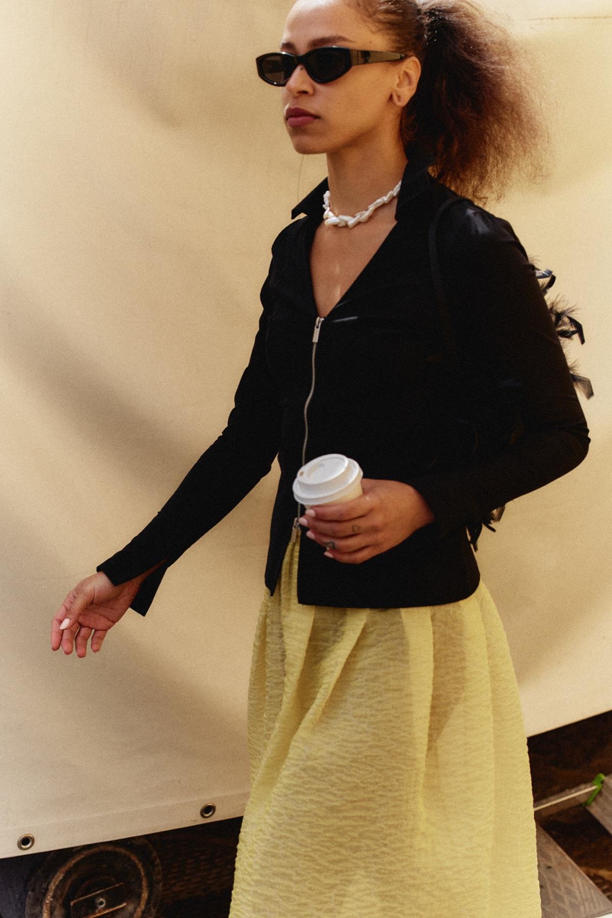 A woman in sunglasses walking with a coffee