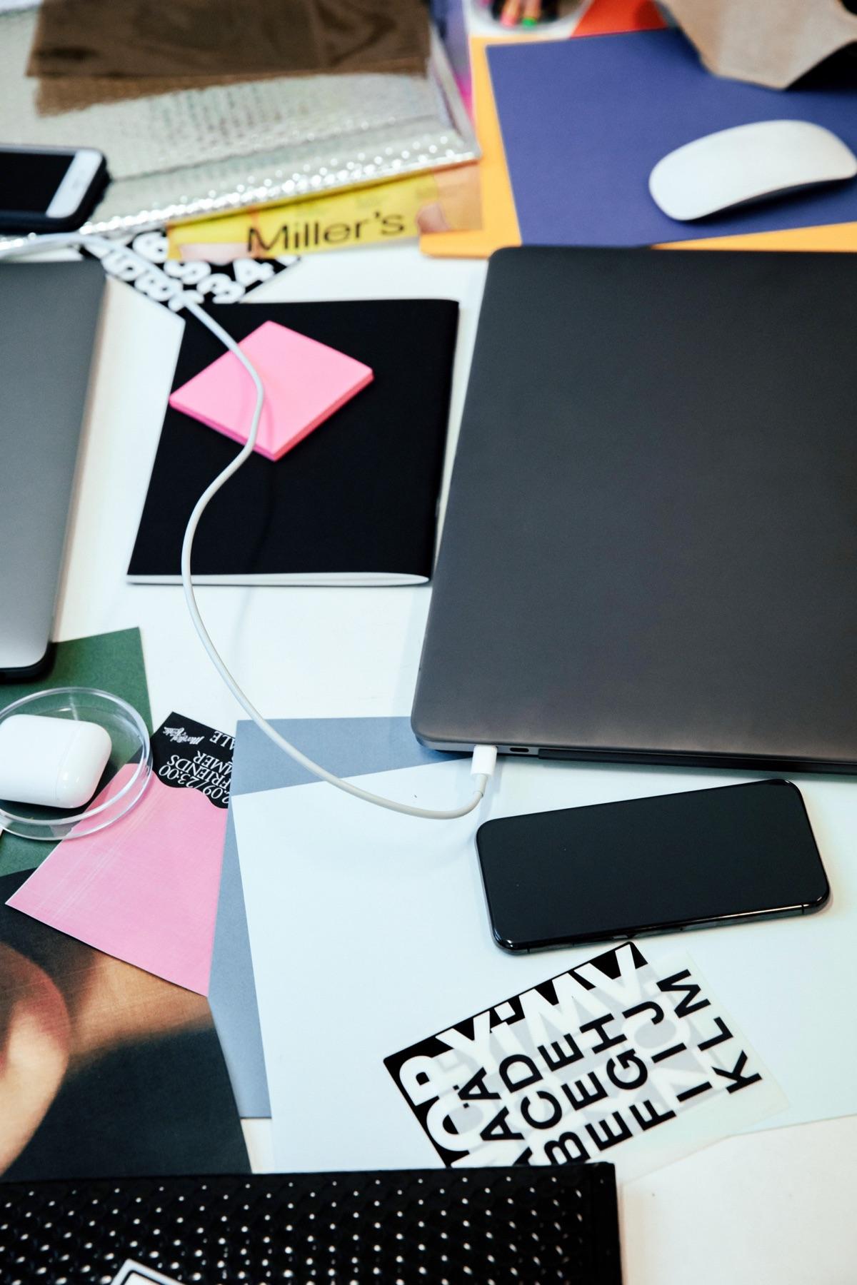 A laptop, phone and printed type samples spread across a desk