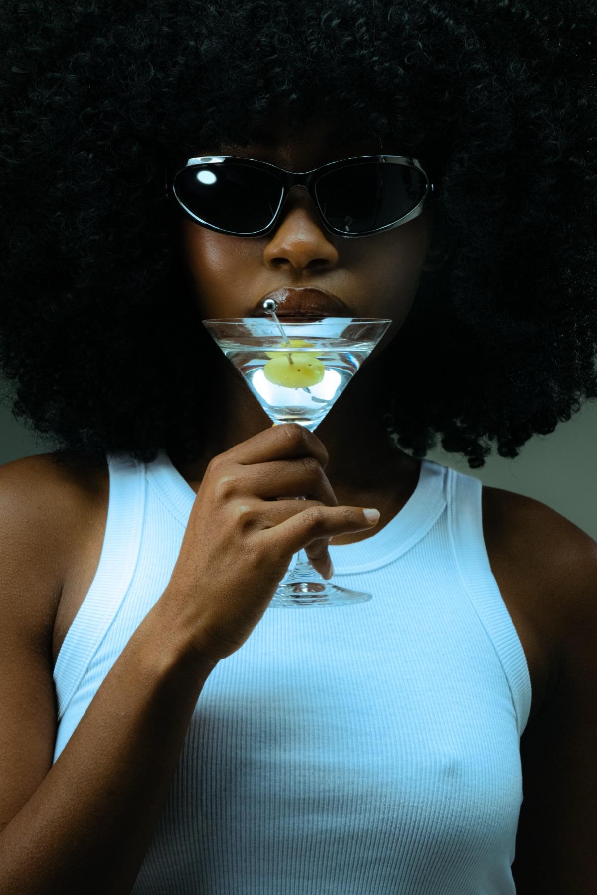 A woman in narrow black sunglasses sipping a martini