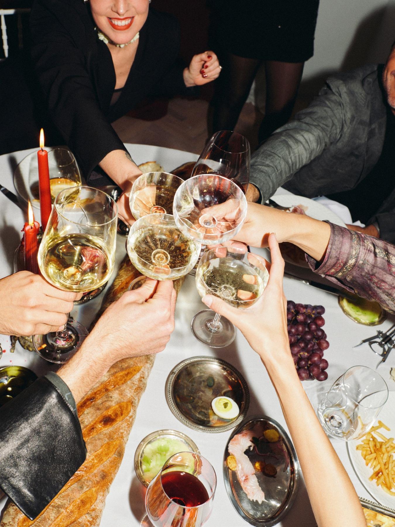 Hands raising glasses of wine over a shared dinner table