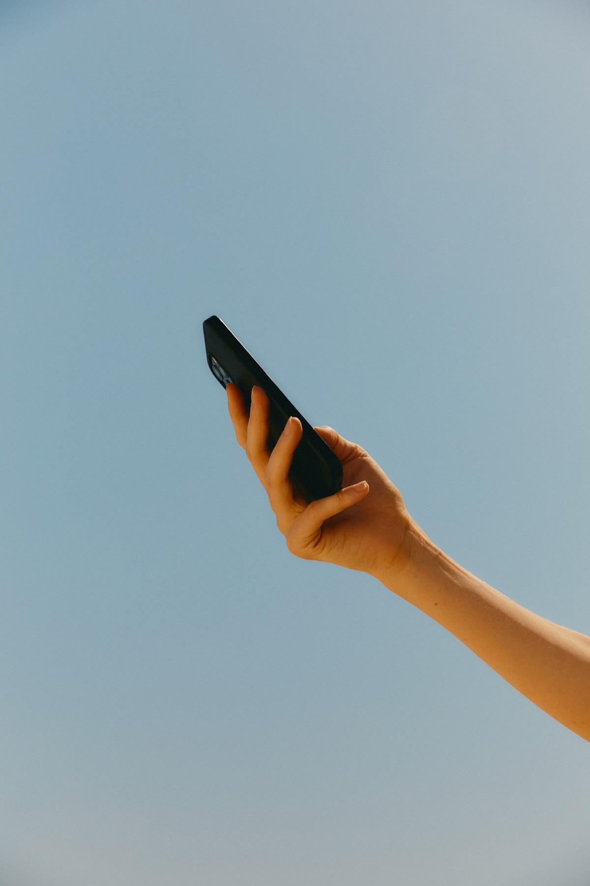A hand holding up a phone against a clear blue sky