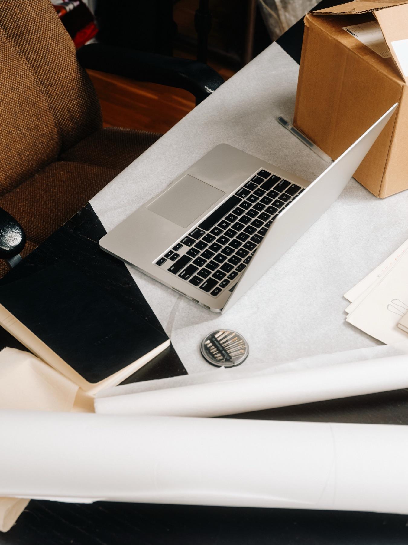 An open laptop on a desk among shipping boxes and packing paper