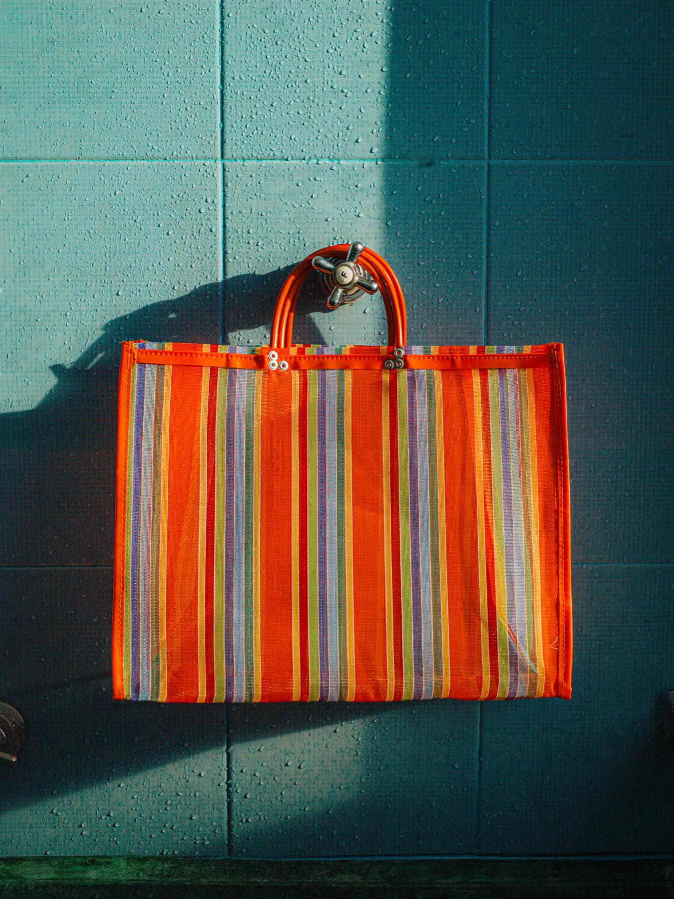 A striped woven market tote hanging on a teal wall