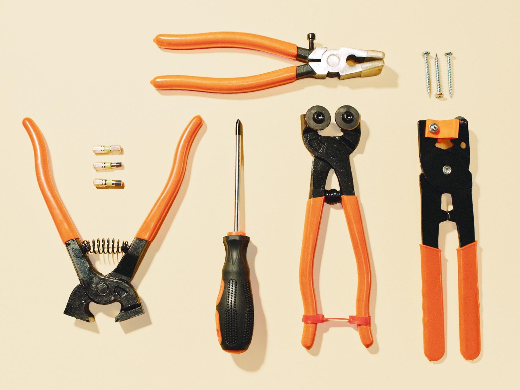 Pliers, a screwdriver and small parts laid out in a row on a cream background