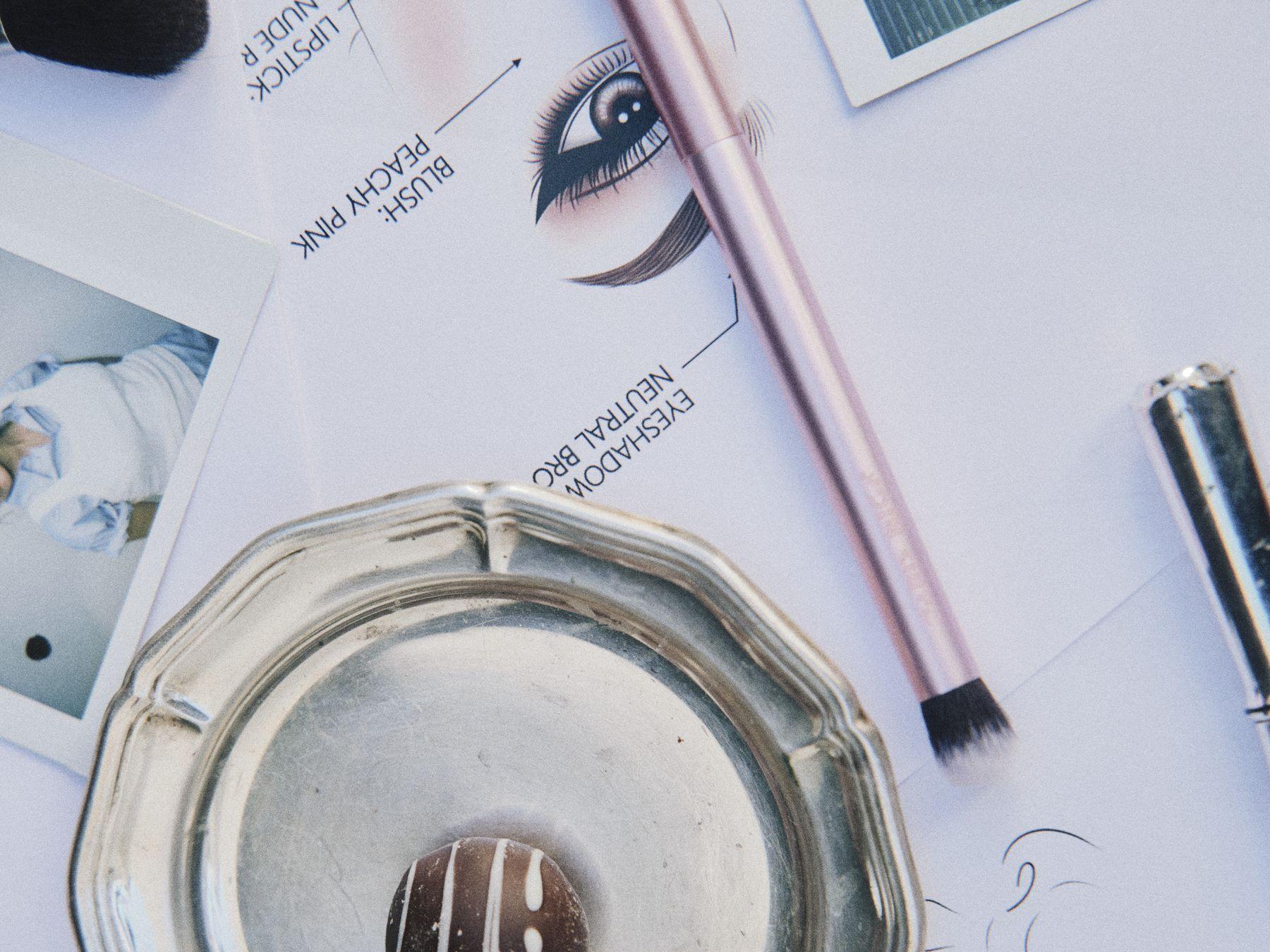A sketch of an eye with makeup brushes and a silver dish
