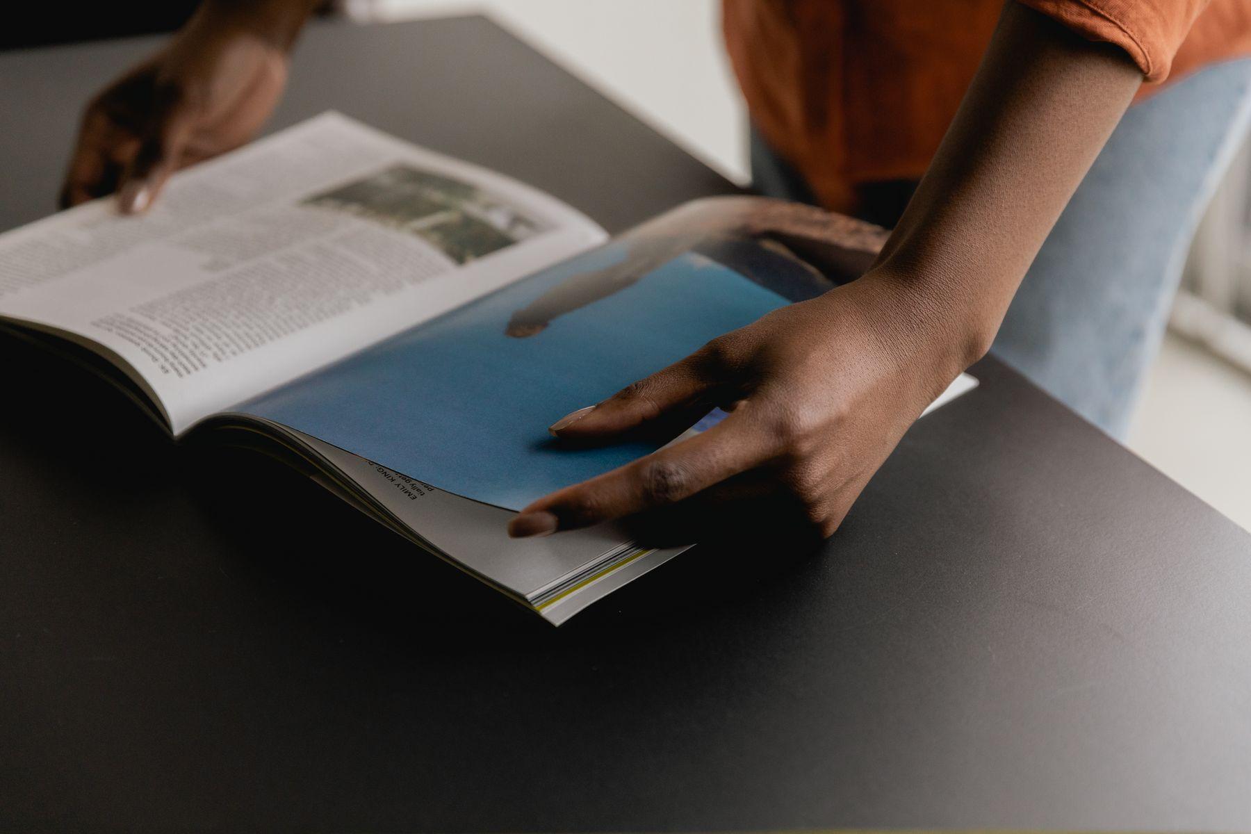 Hands turning the pages of a magazine on a dark table