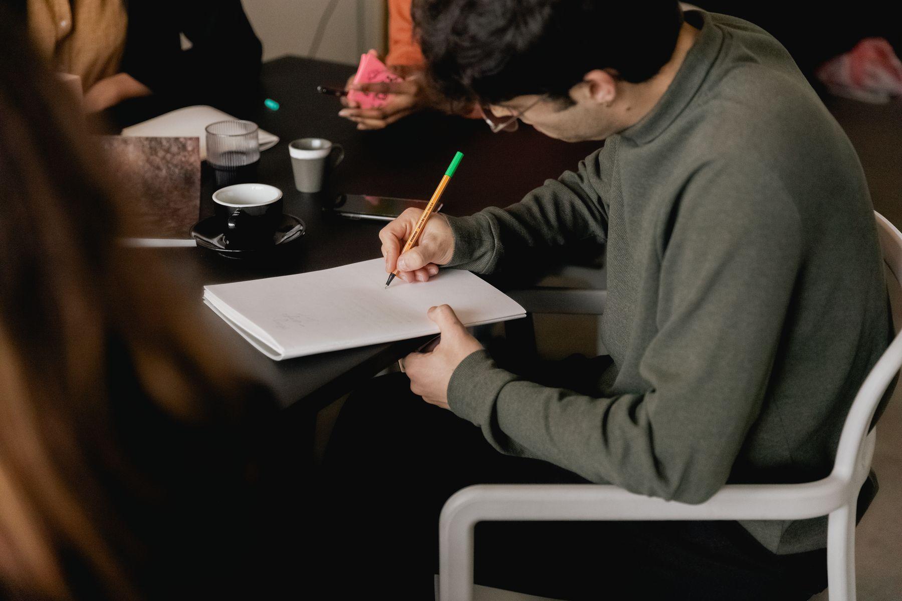 A person writing in a notebook at a dark table