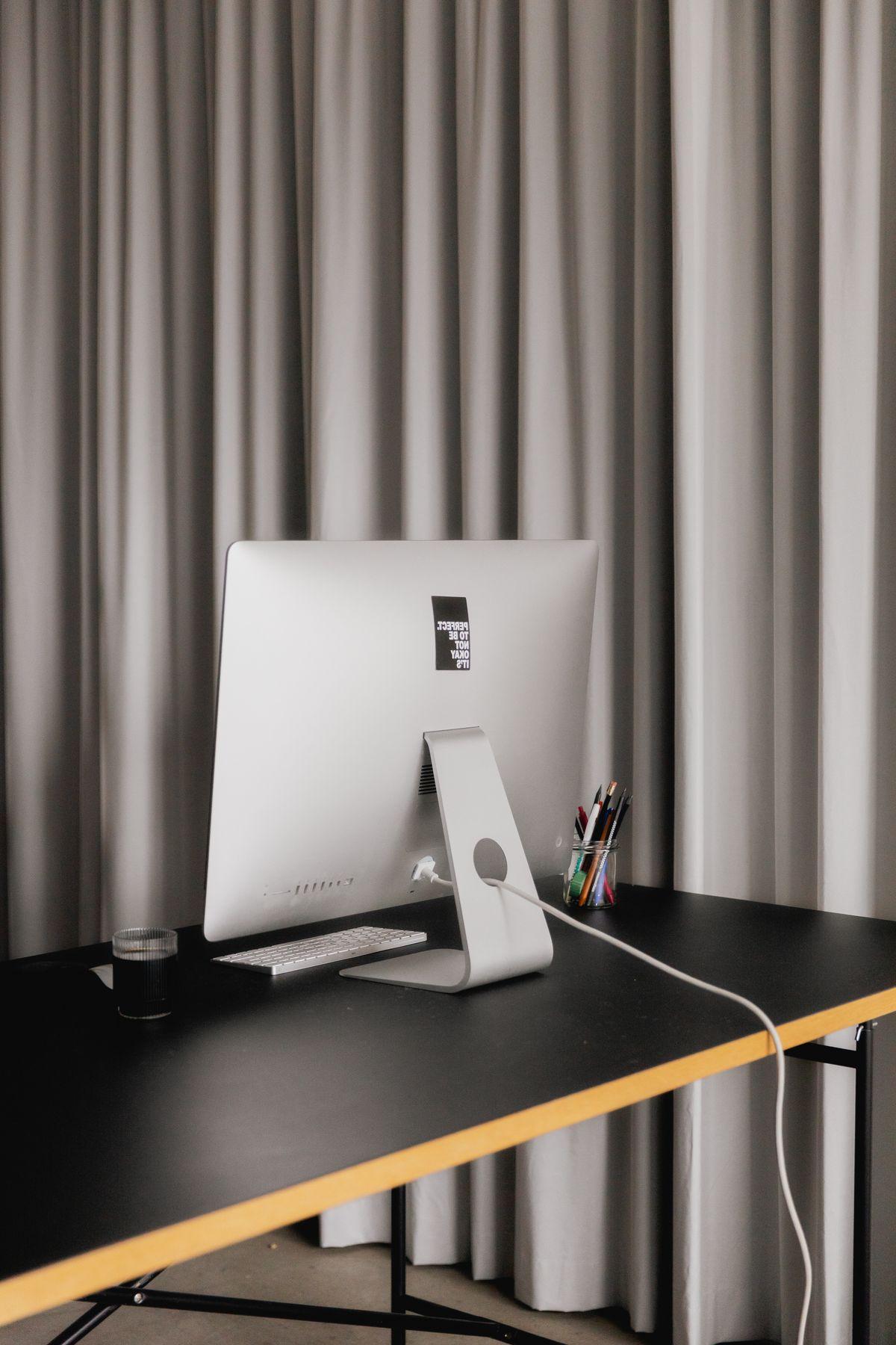 A desktop computer on a clean desk by a curtain