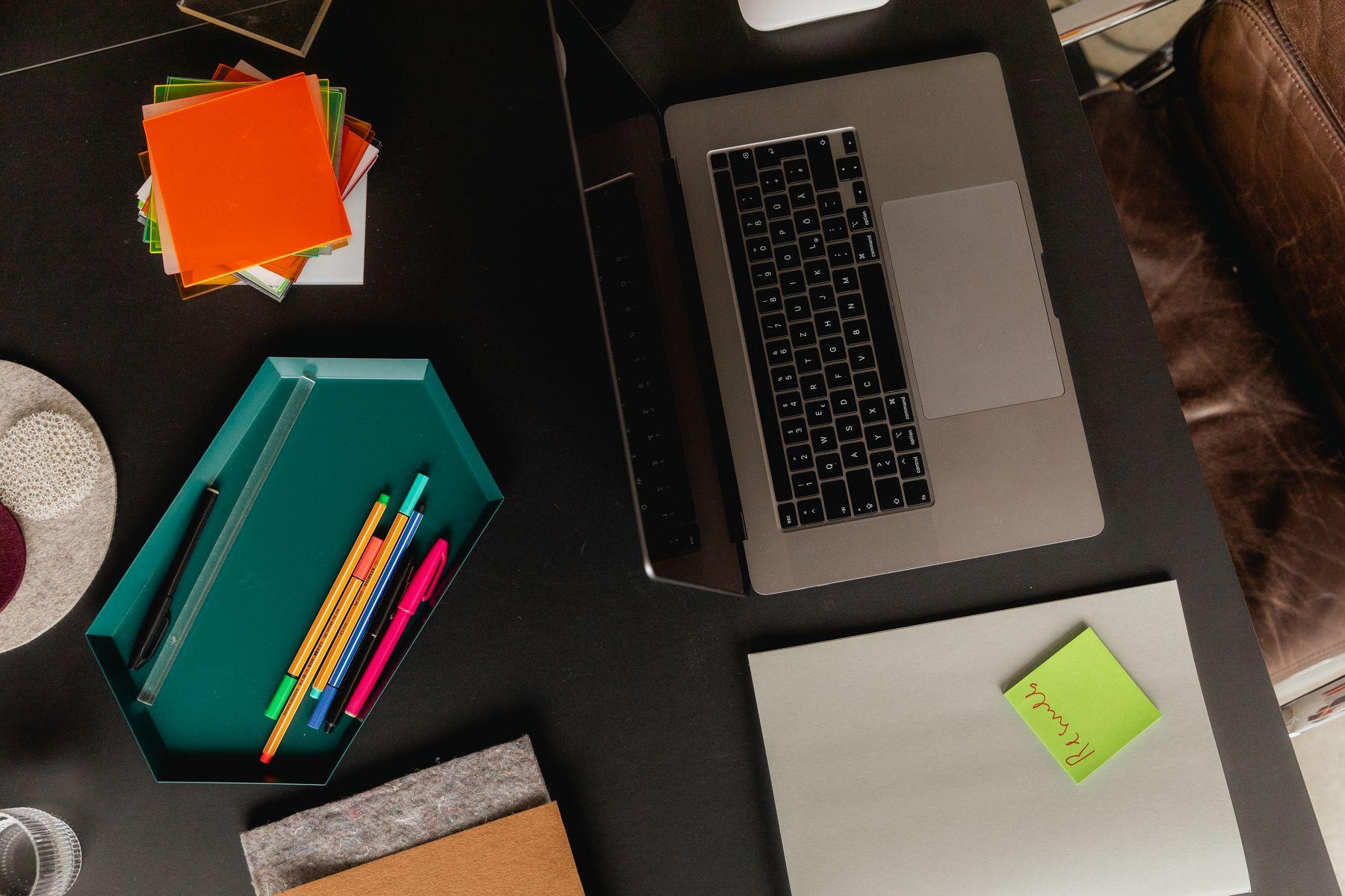 A desk from above with swatches, markers, a ruler and a laptop