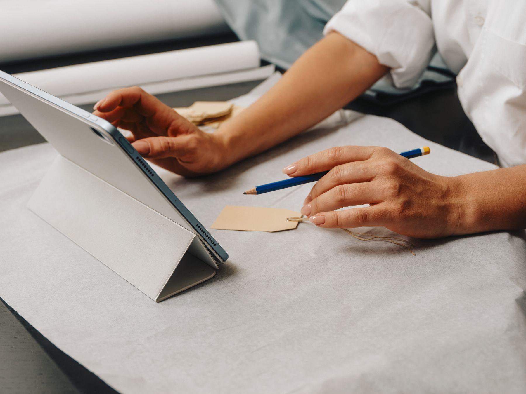 A hand writing notes beside a tablet on a white table