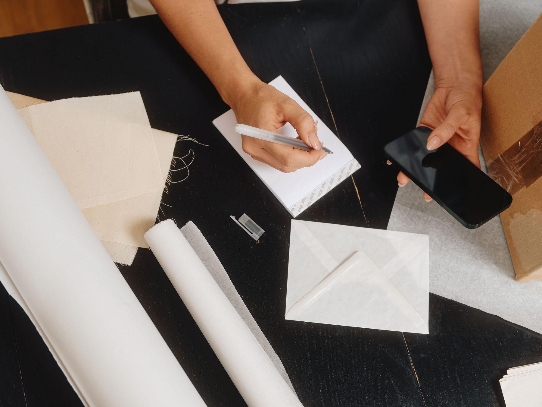 Hands with an envelope, paper rolls and a phone on a work table