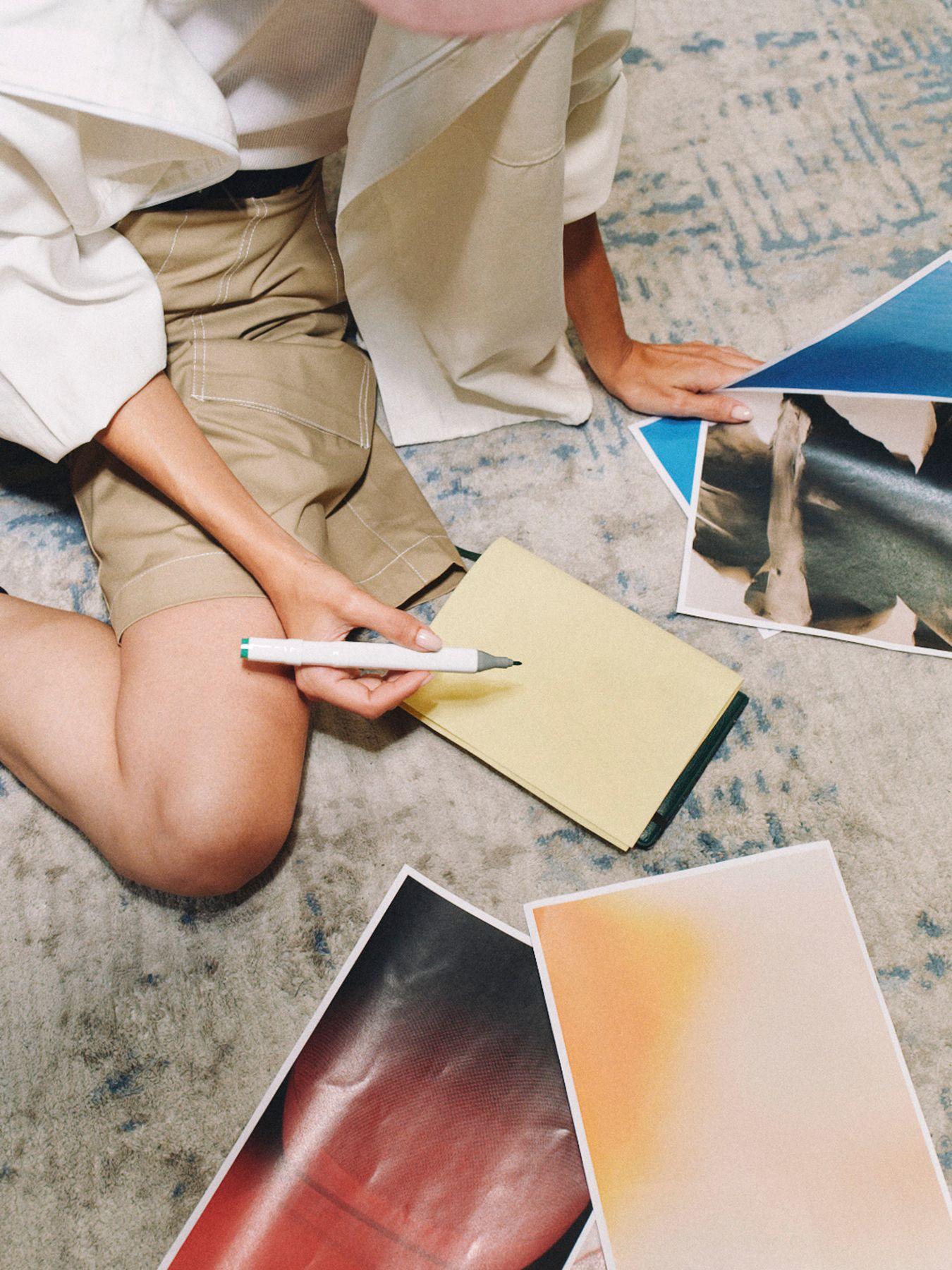 Printed photos spread on a rug around a seated person