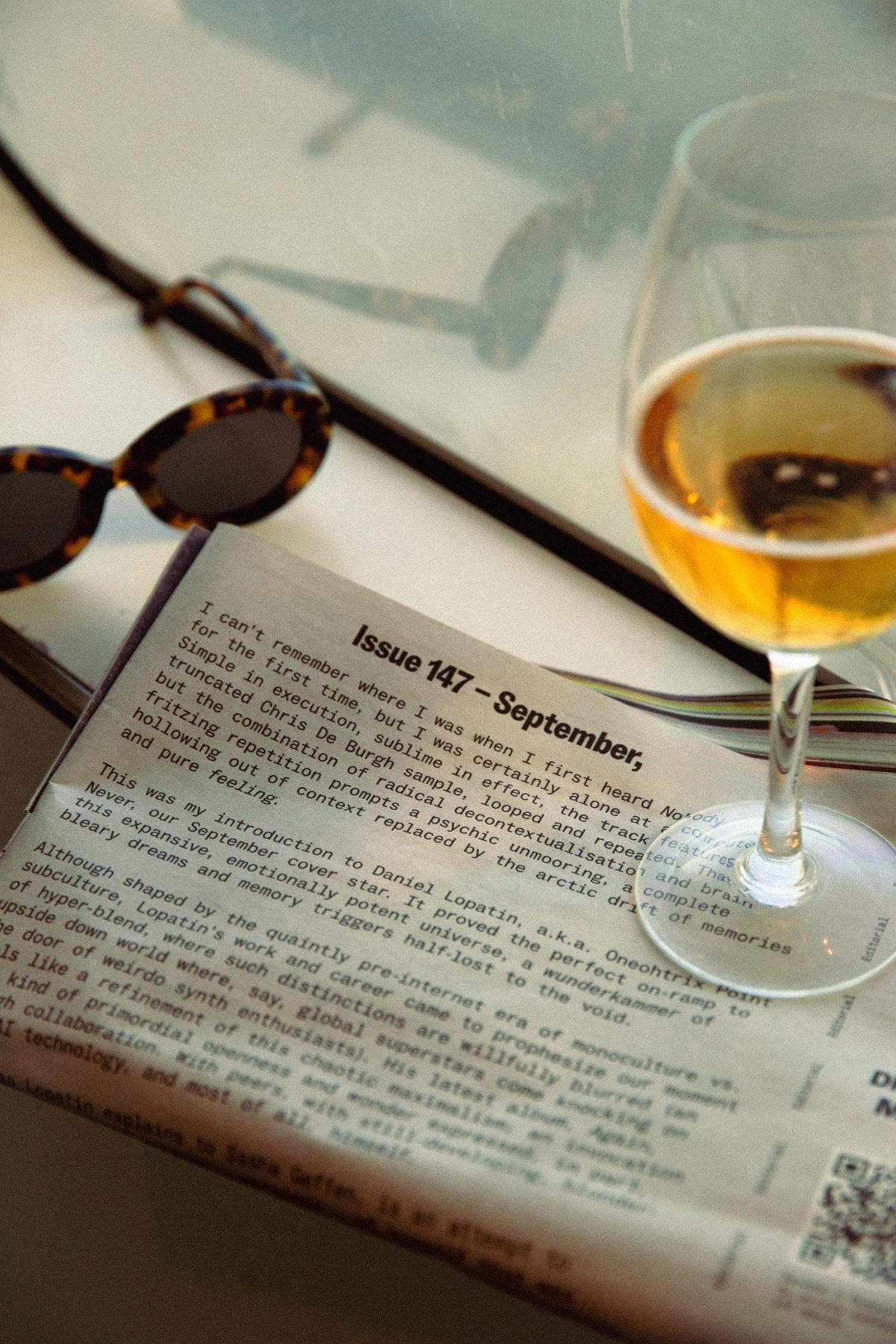 Sunglasses, a newspaper and a glass of wine on a table