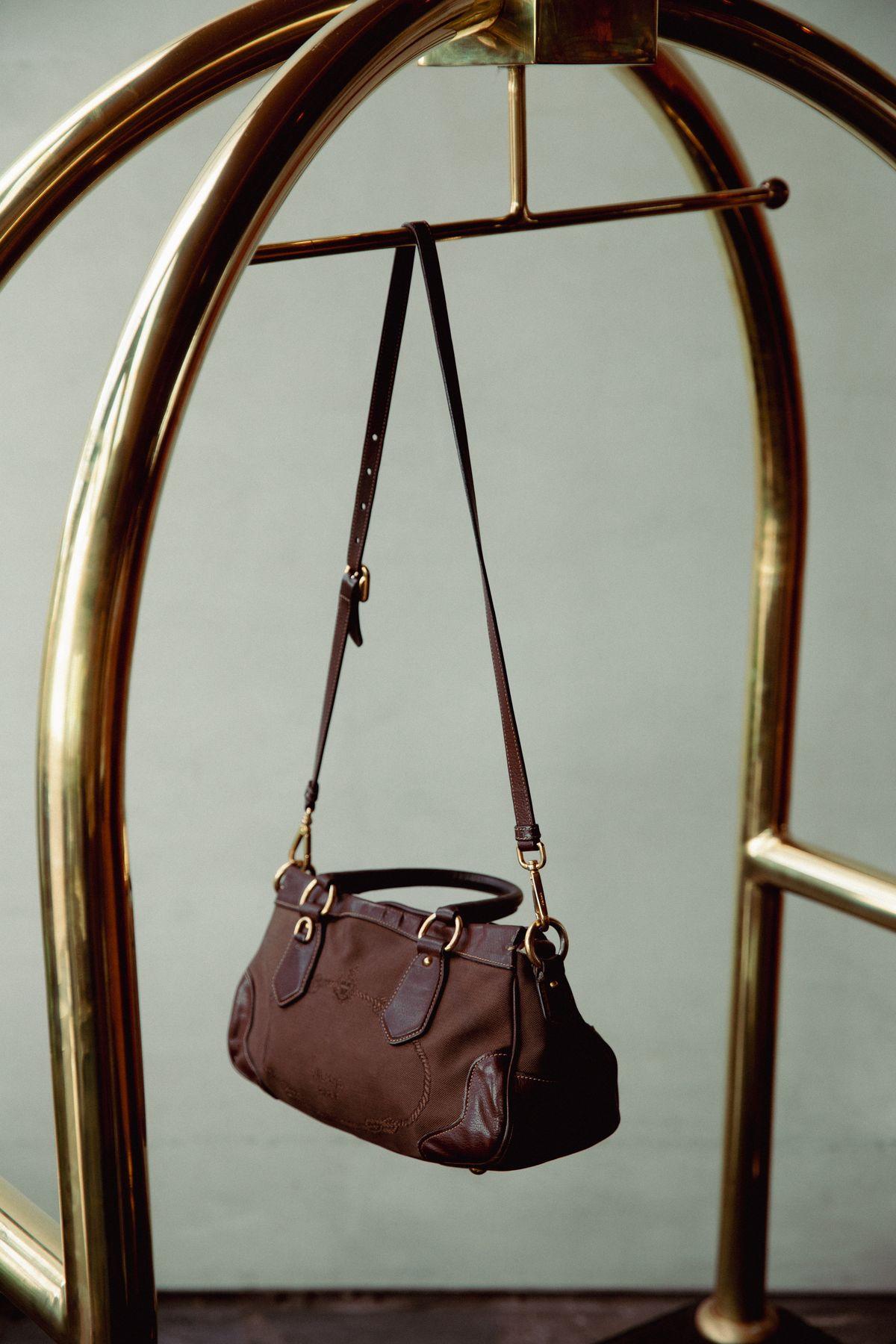 A leather bag hanging from a brass luggage cart
