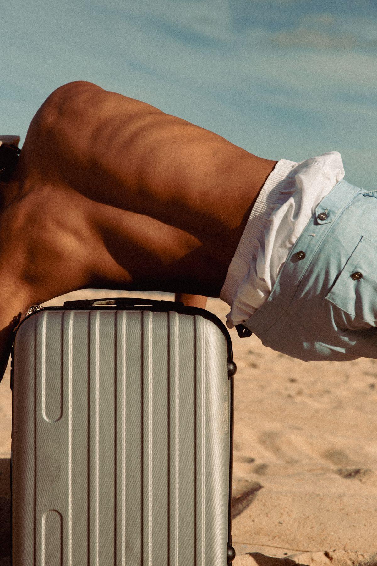 An arm resting on a silver suitcase on the sand