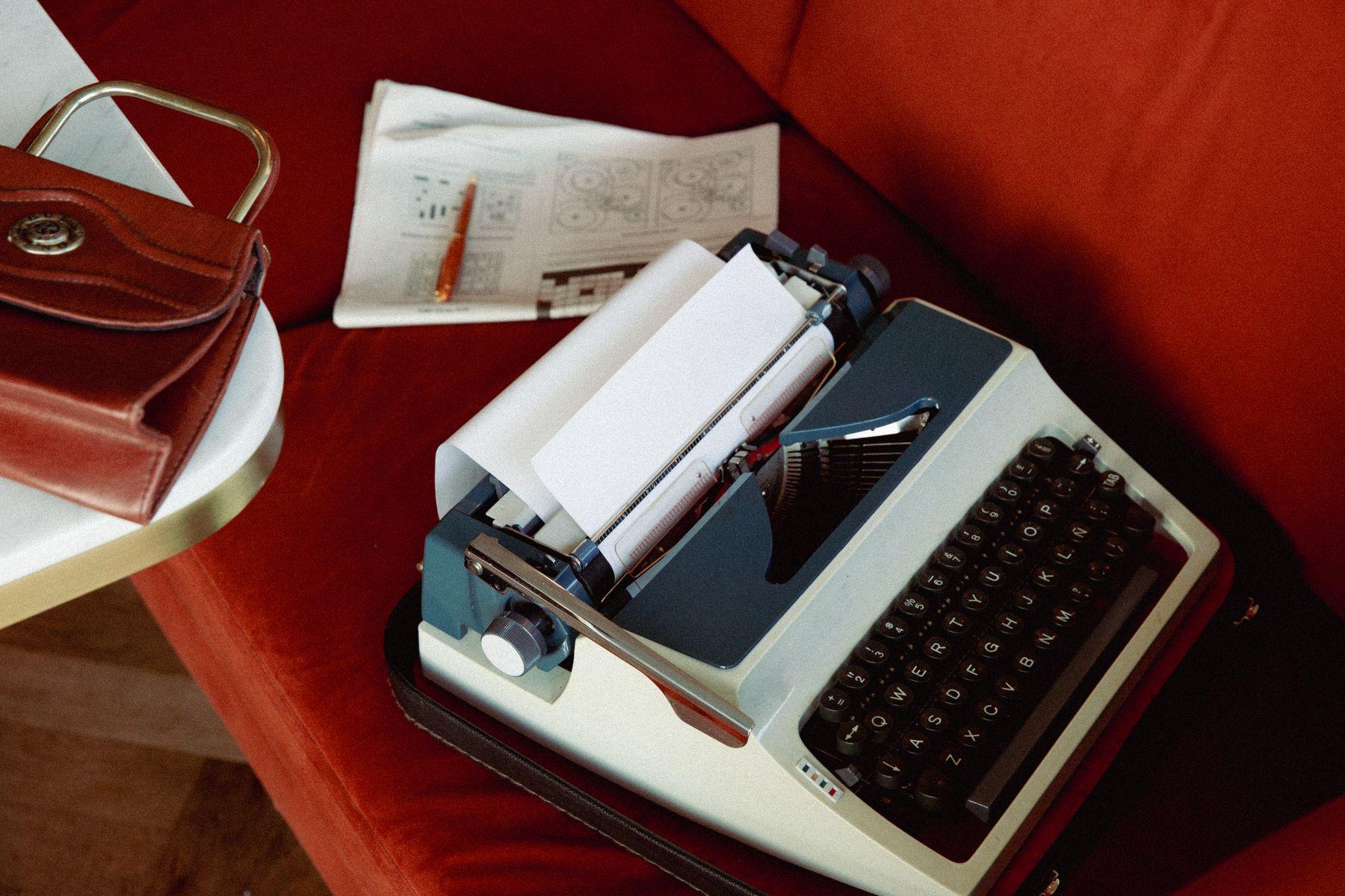 A typewriter, a leather bag and papers on a red sofa