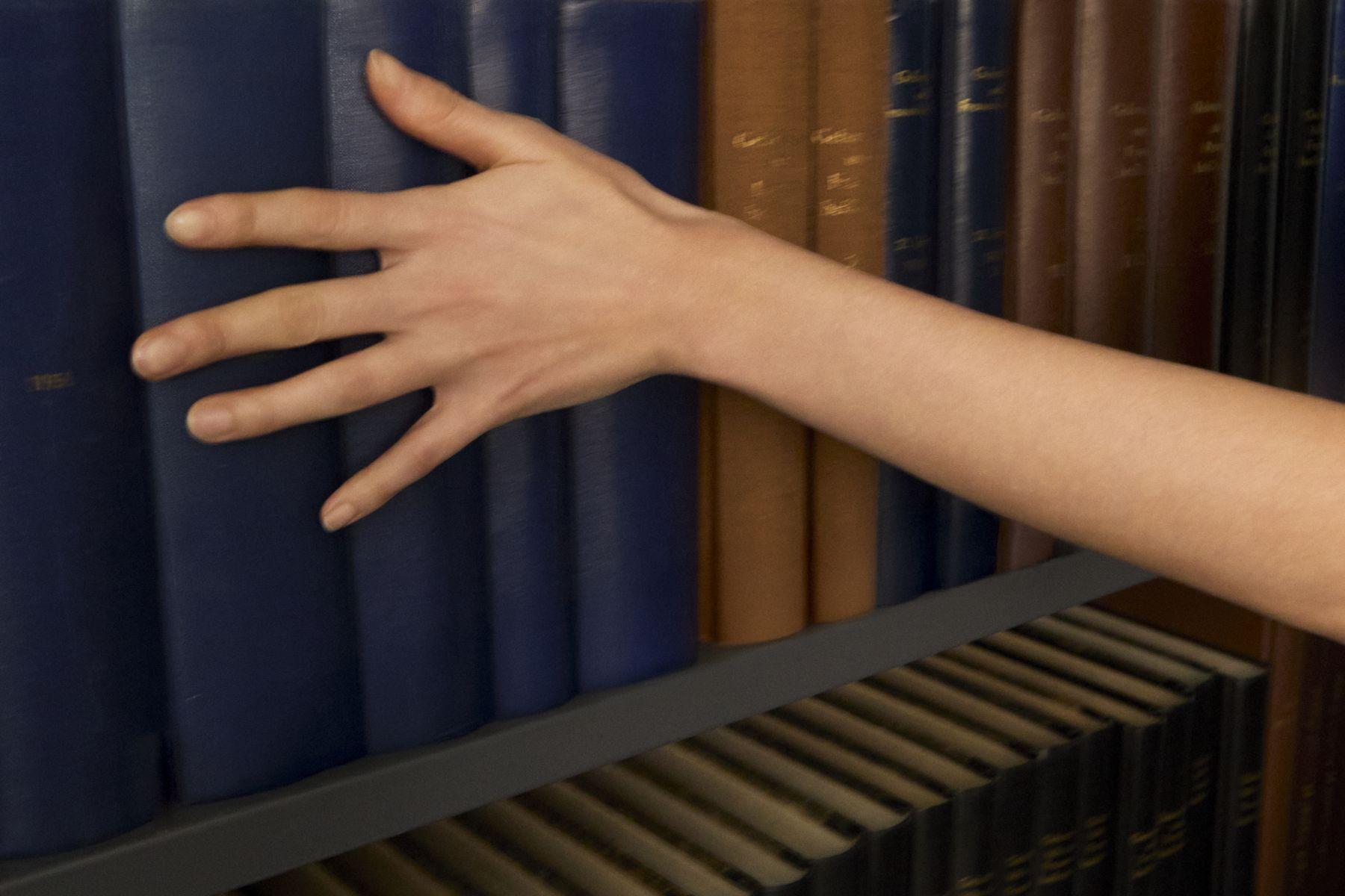 A hand reaching along a shelf of library books