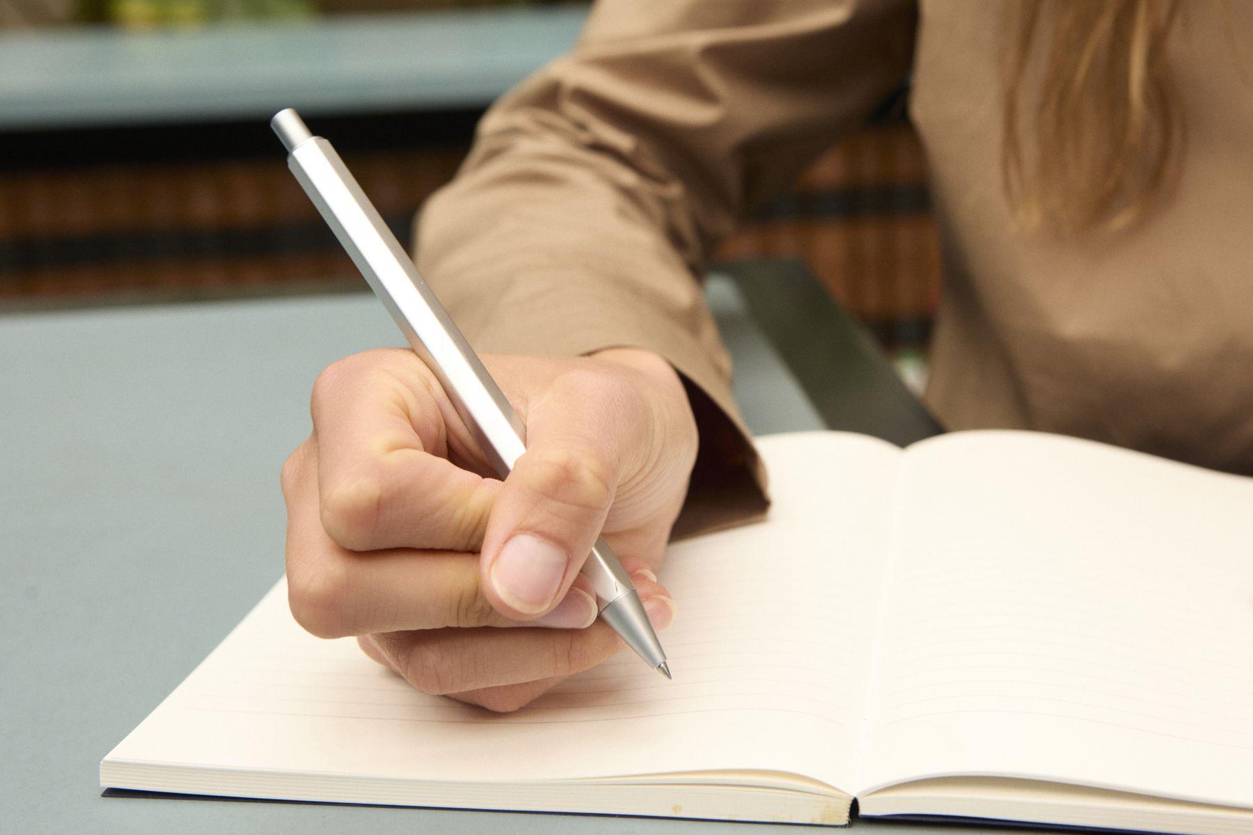 A hand writing with a pen in an open notebook