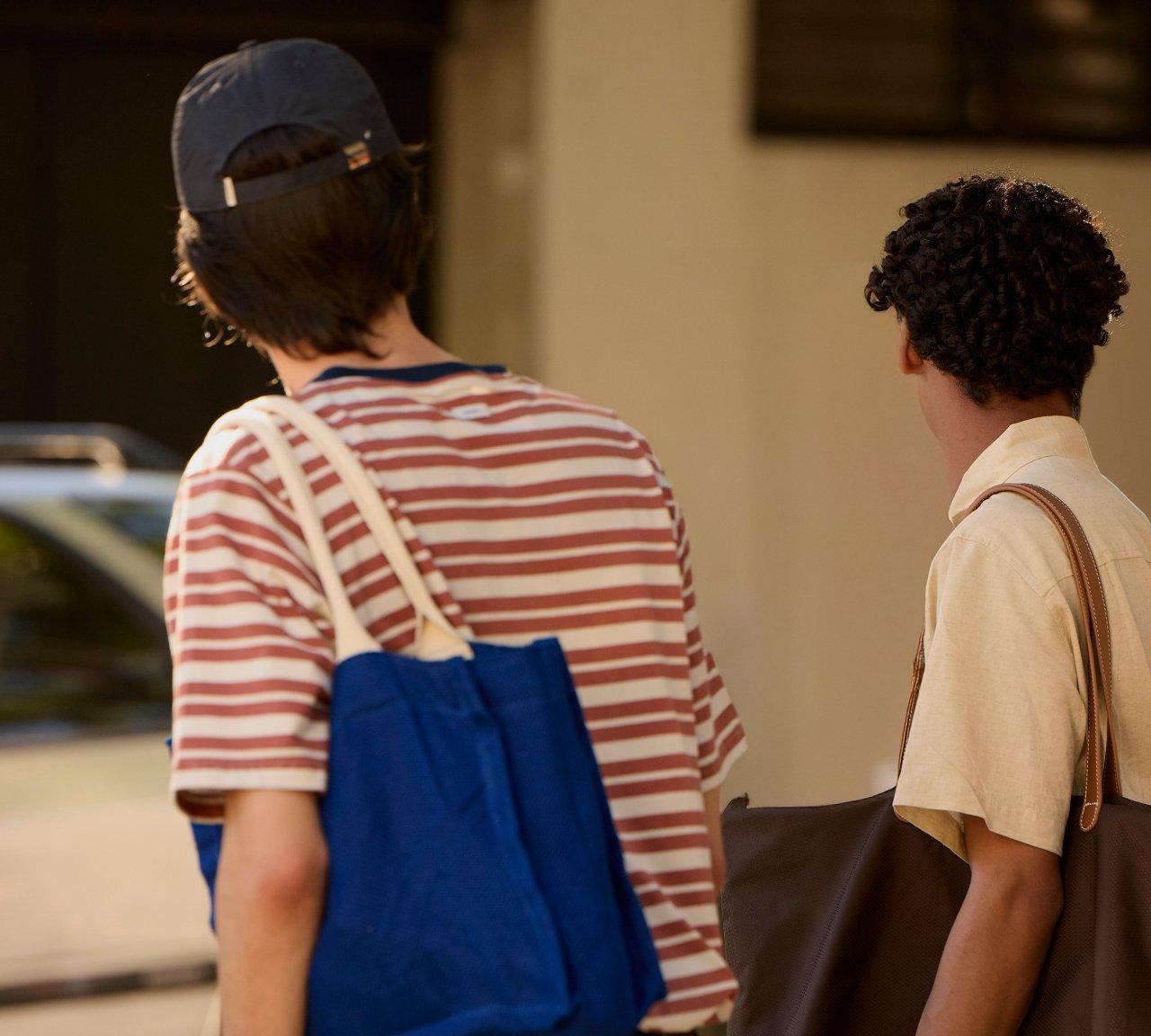 Two friends with tote bags on their shoulders walking down a sunny street