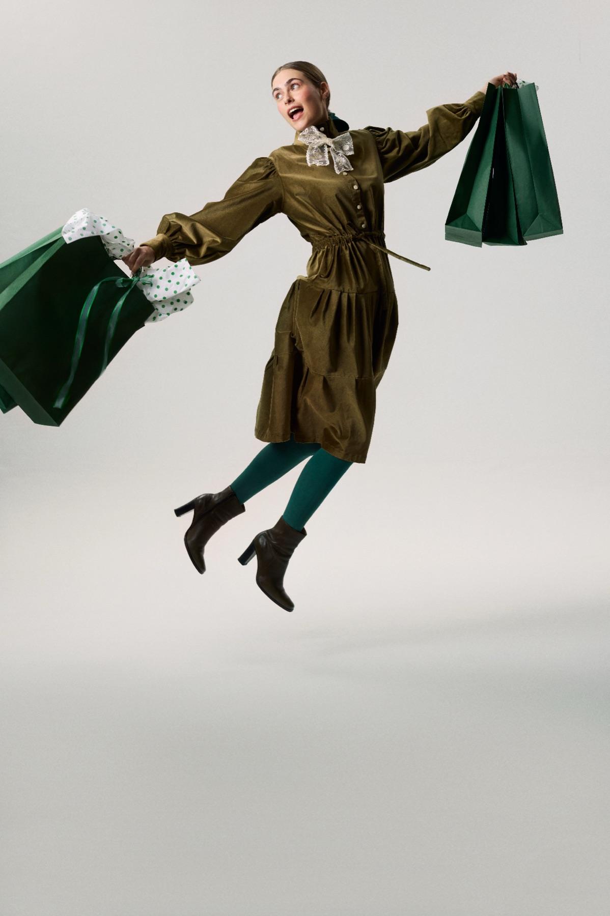 A woman leaping with green shopping bags in both hands