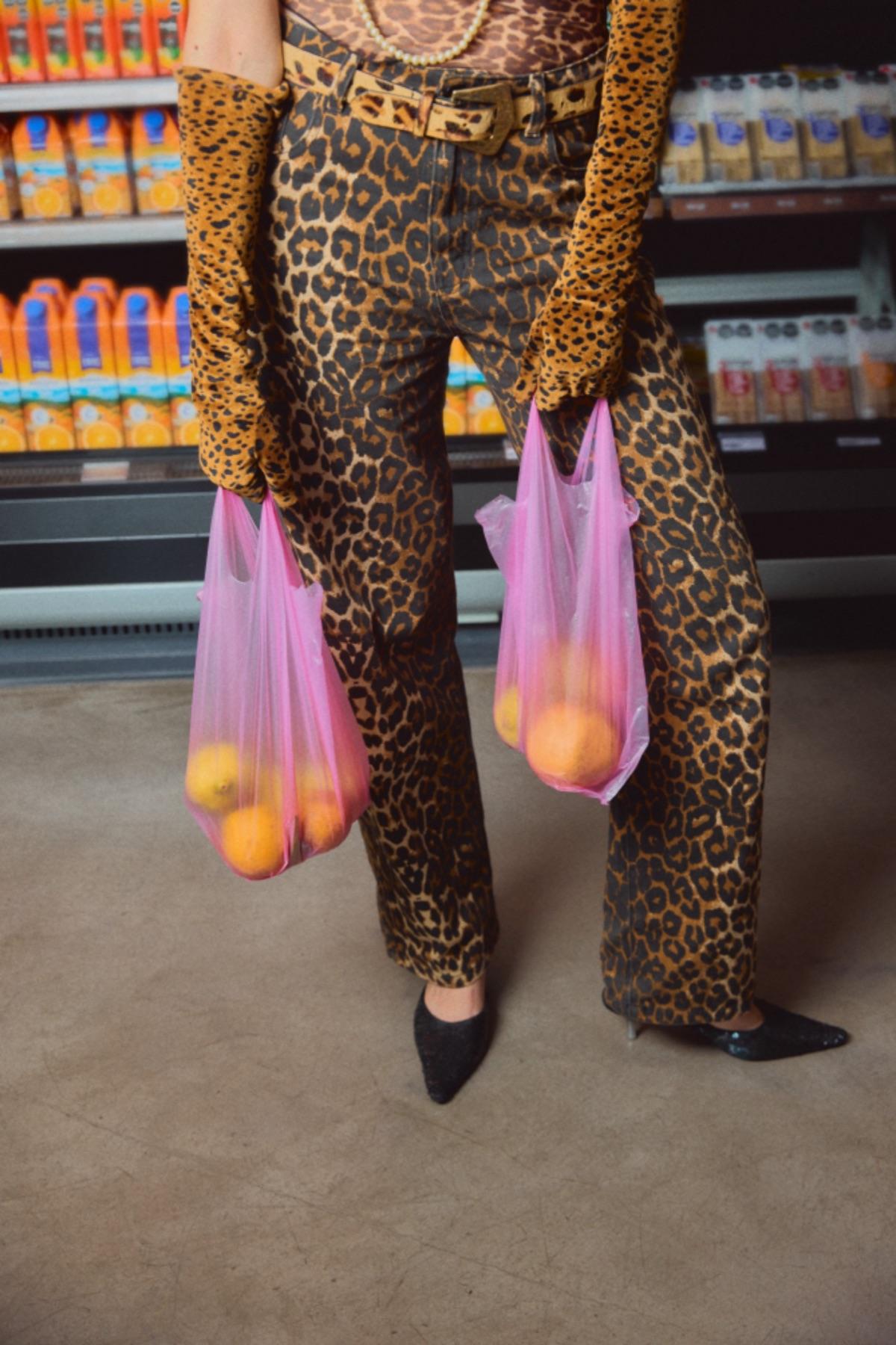 A shopper in leopard-print trousers carrying two bags of oranges