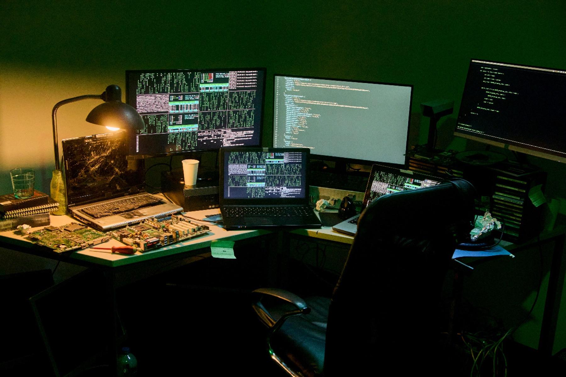 A developer's desk with several monitors showing code in a dark room
