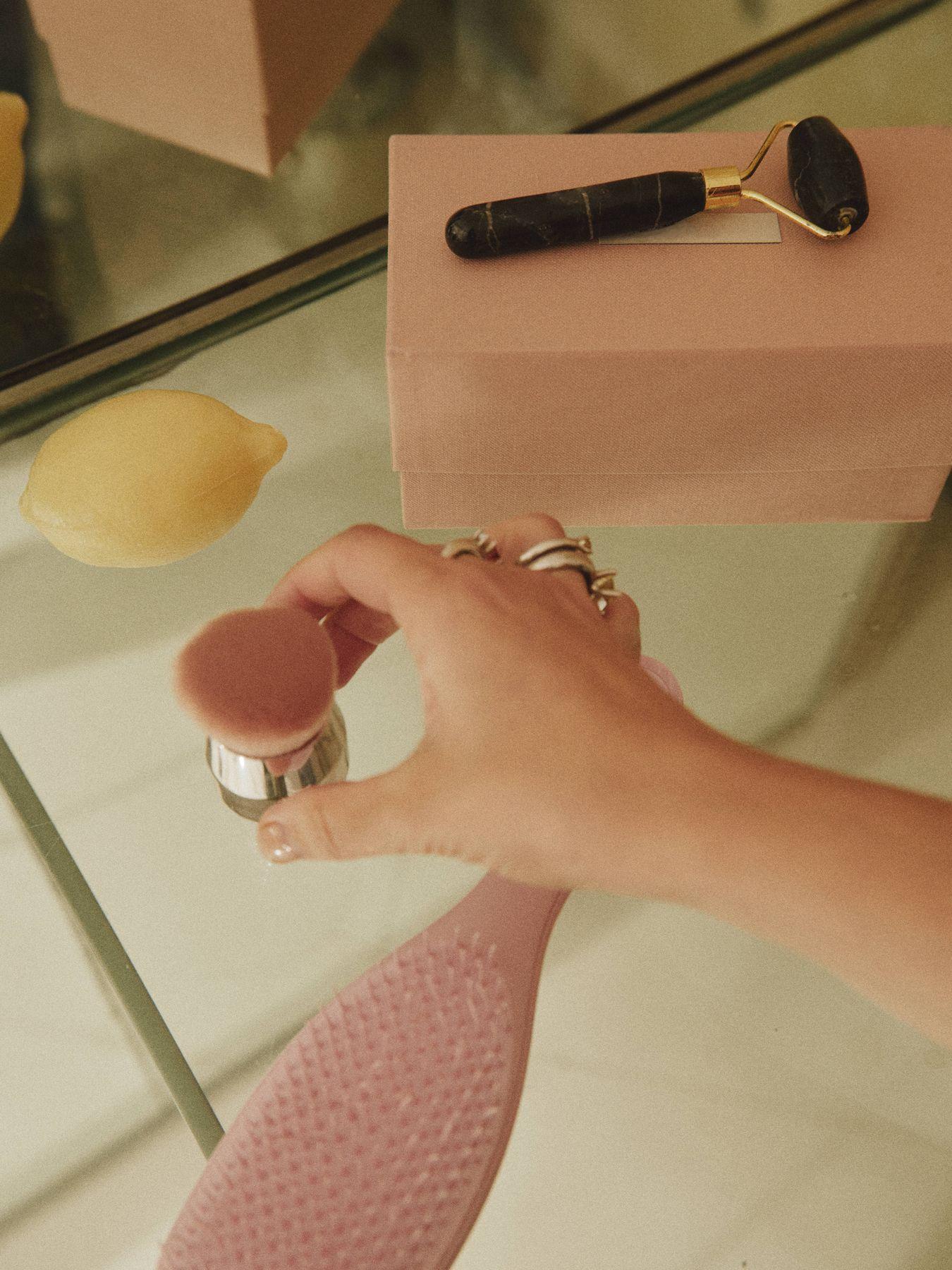 A hand holding a beauty tool beside a pink box