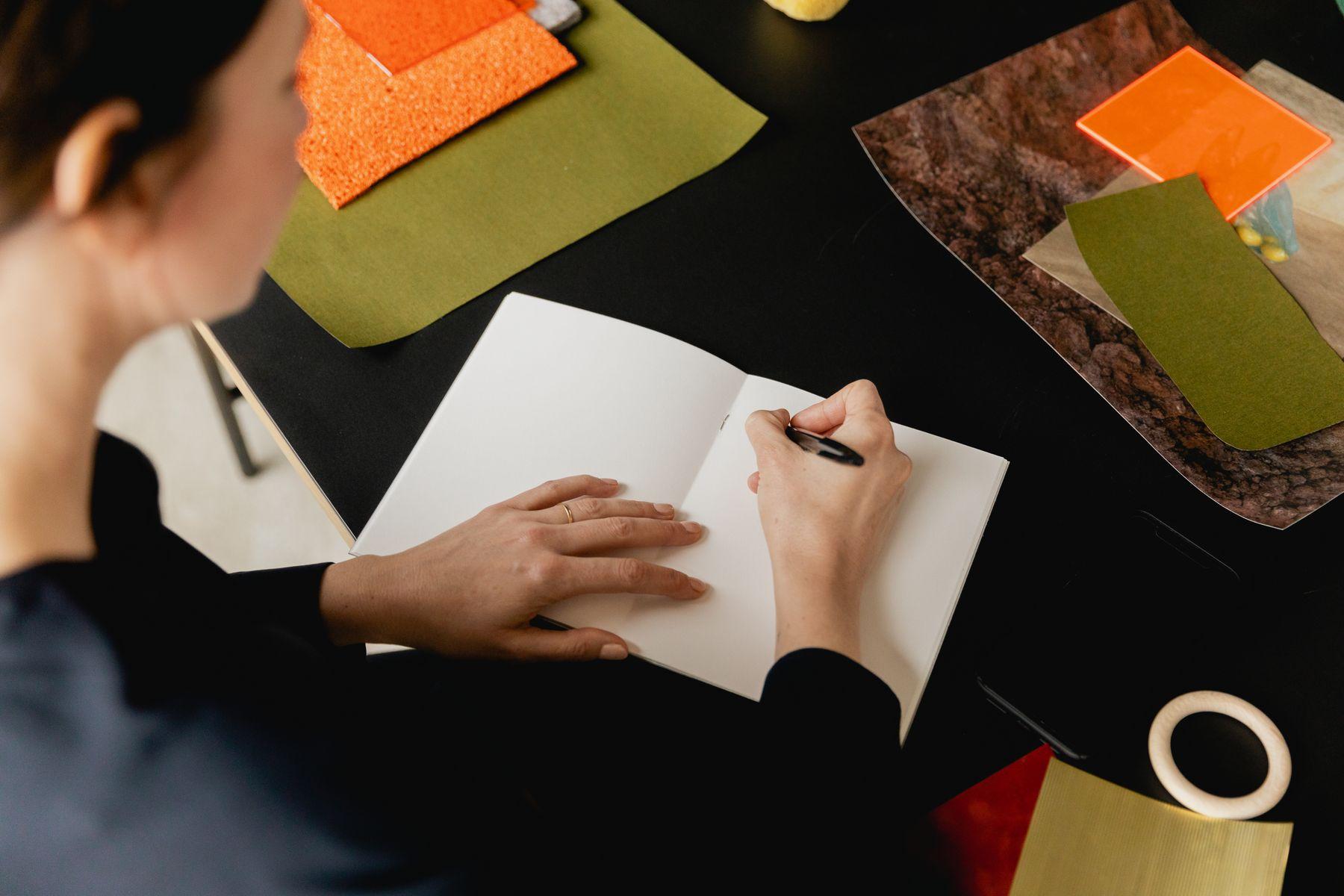 Hands writing on paper beside fabric and material samples
