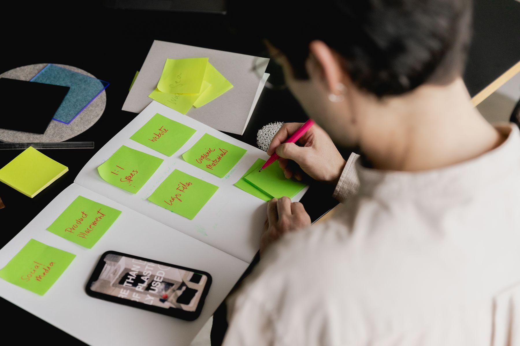 A hand writing on rows of green sticky notes