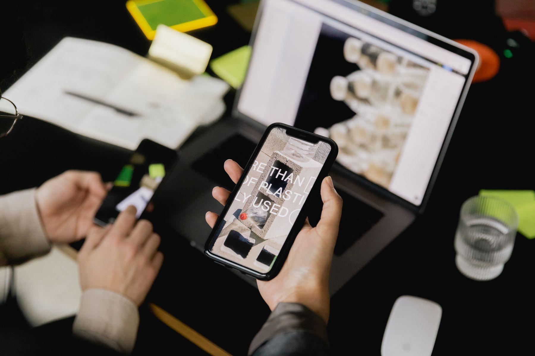 A hand holding a phone beside a laptop showing product pages