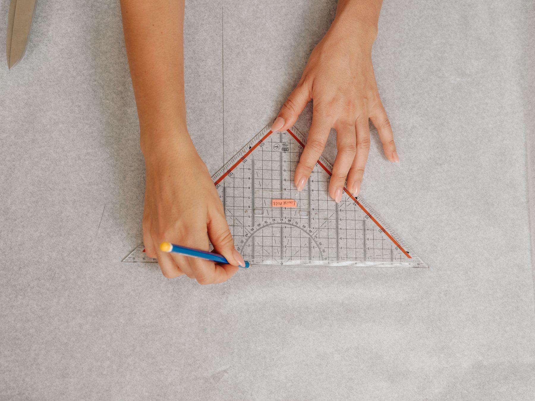 Hands drawing lines with a ruler on a large sheet of paper