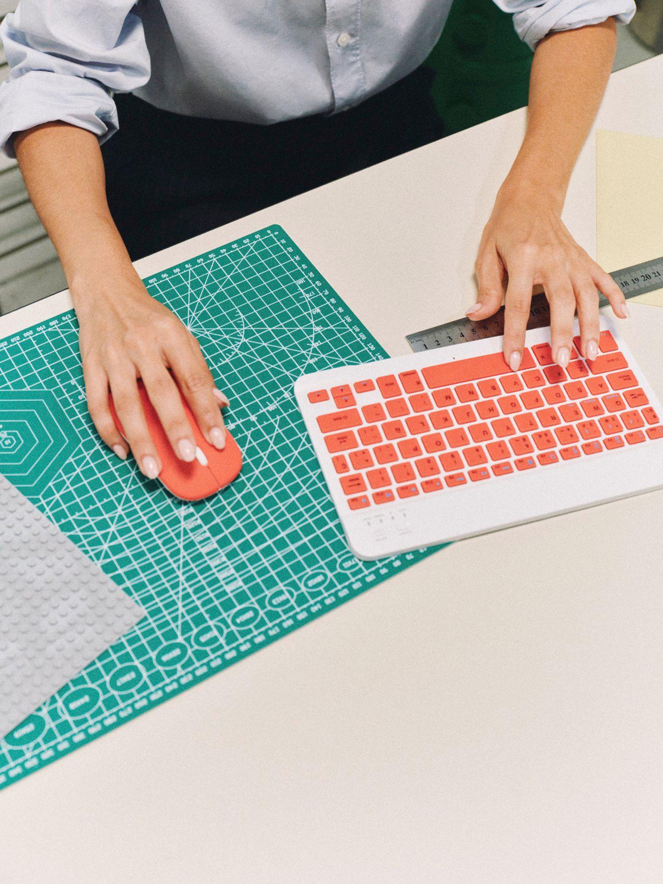 Hands using a colorful keyboard and mouse on a cutting mat