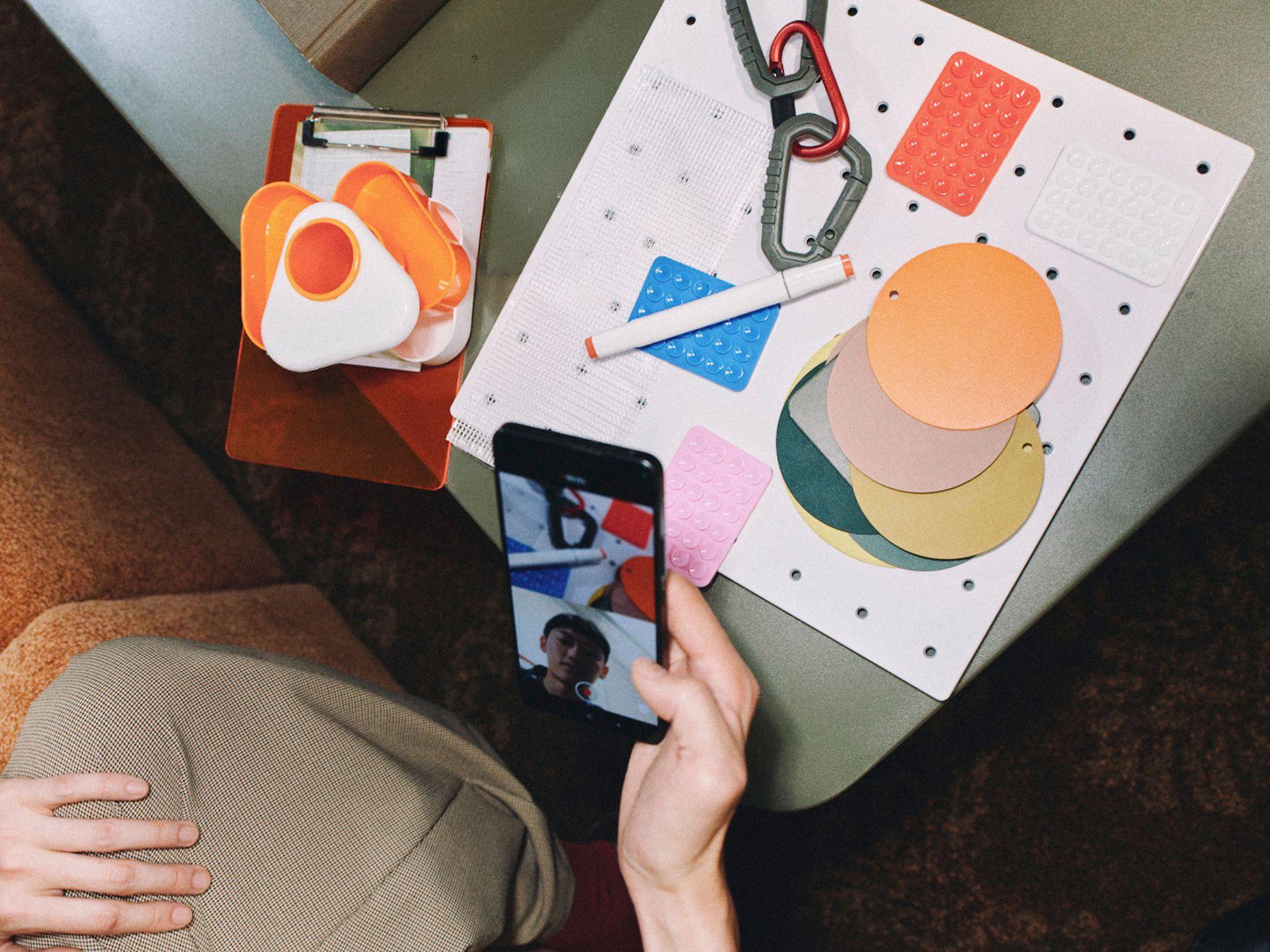 A hand holding a phone over a table of colored shapes