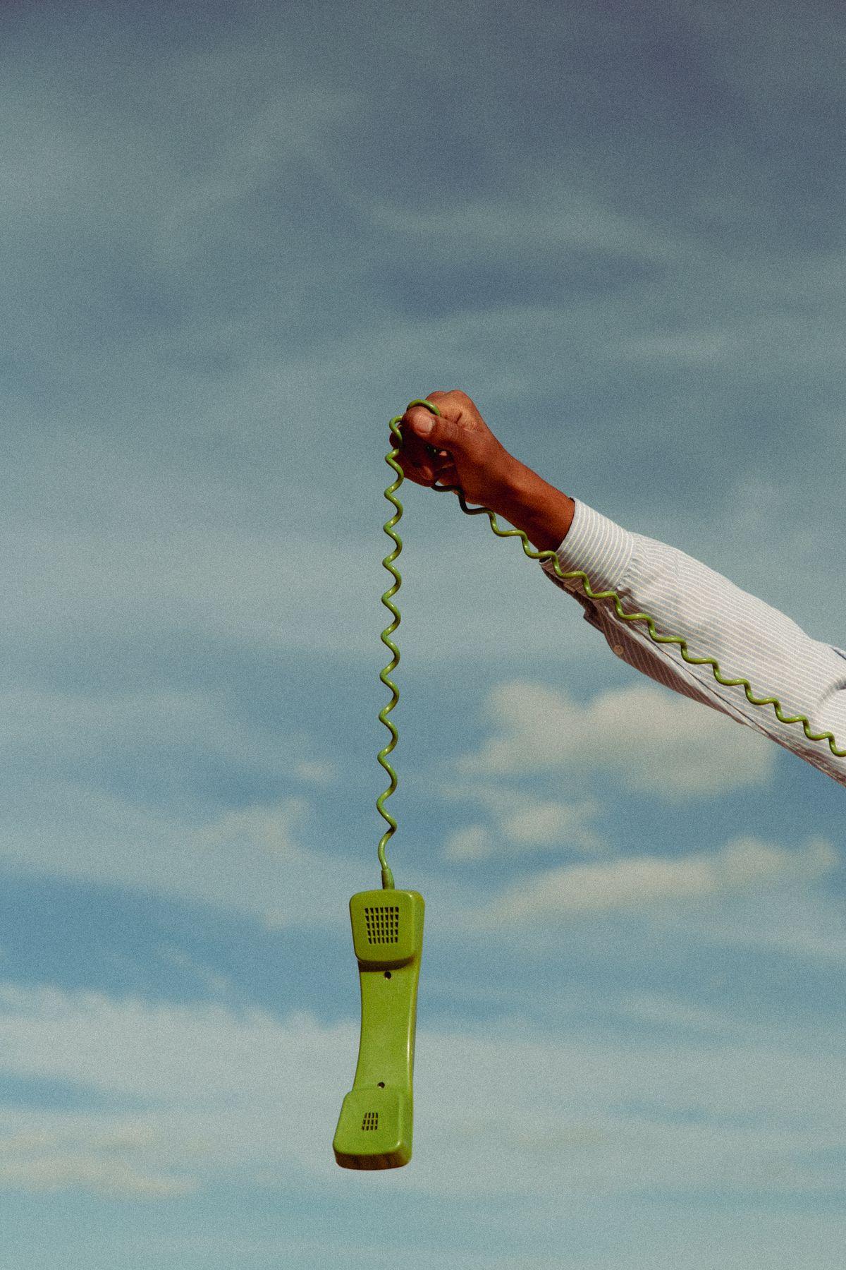 A green phone receiver hanging on its cord against the sky