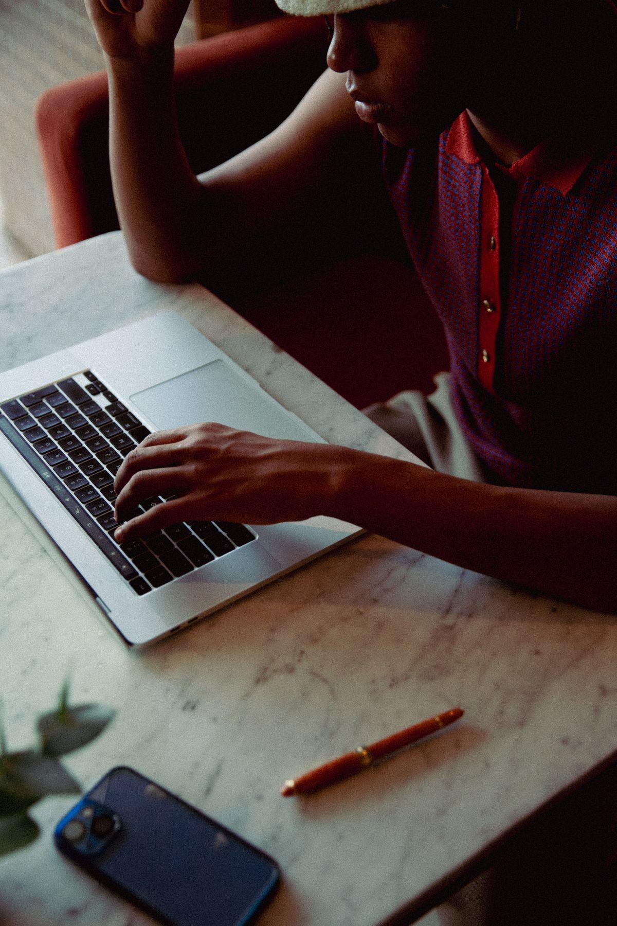 Hands typing on a laptop on a marble table beside a phone